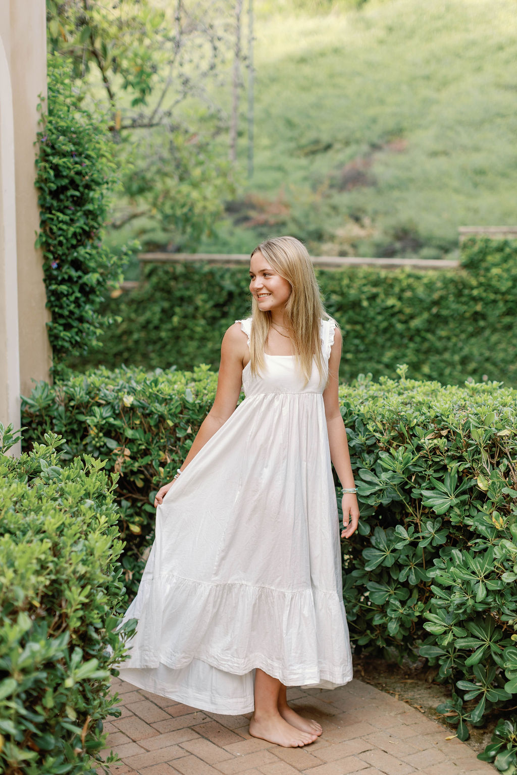 A sibling smiling and in a white dress barefoot for a family photo at Pelican Hill  California.