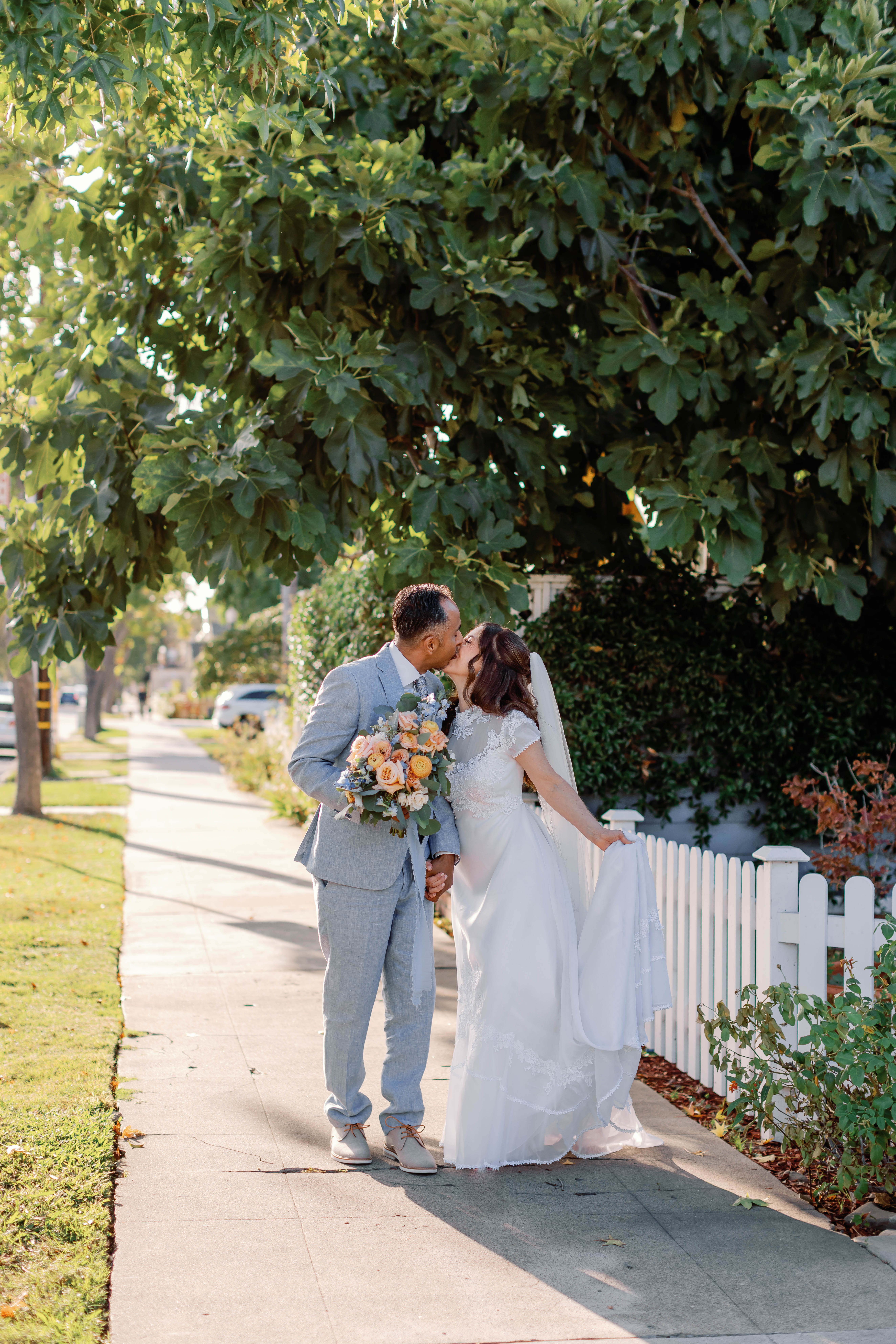 Bride and groom kiss in front of the white fence Chapel of Orange wedding | Photo by Sarah Block Photography