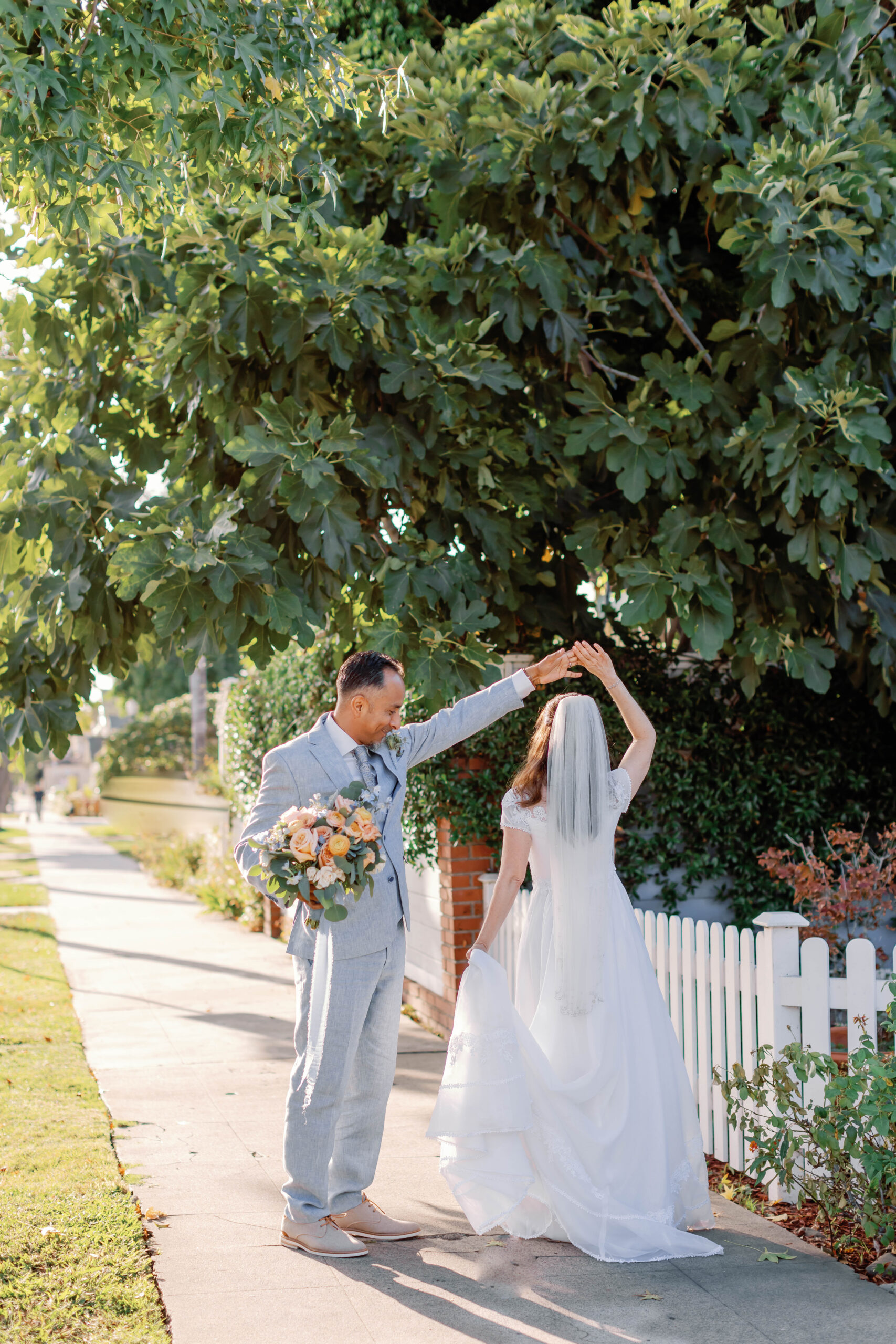 Bride and Groom twirl on the sidewalk in front of a fence in the sunlight | Photo by Sarah Block Photography