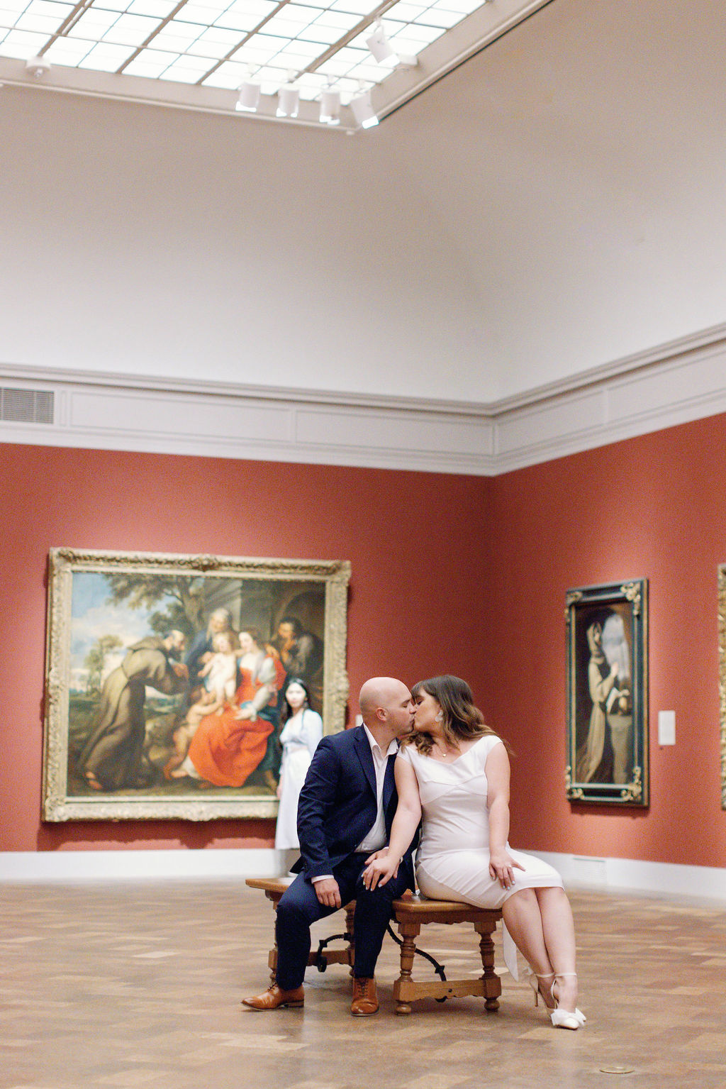 Engagement photo of Jimmy and Hannah  kissing on a bench surrounded by art at San Diego Museum of art. |Photo by California Photographer Sarah Block Photography