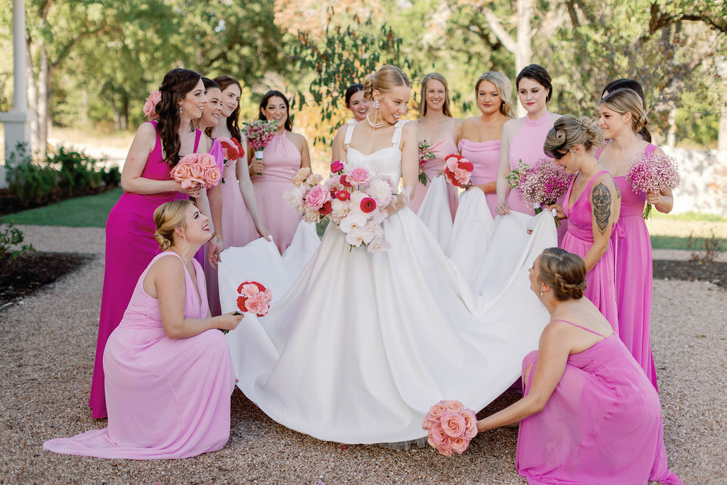 Bride stands holding her brilliant pink bouquet while her bridesmaids are standing around her dressed in brilliant shades of pink. | Photo by Texas Photographer Sarah Block Photography